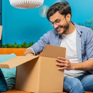 A man sitting on the couch opening up a box.