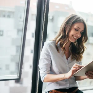 A woman is smiling while holding her tablet.