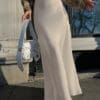 Woman in beige skirt holding white bag.